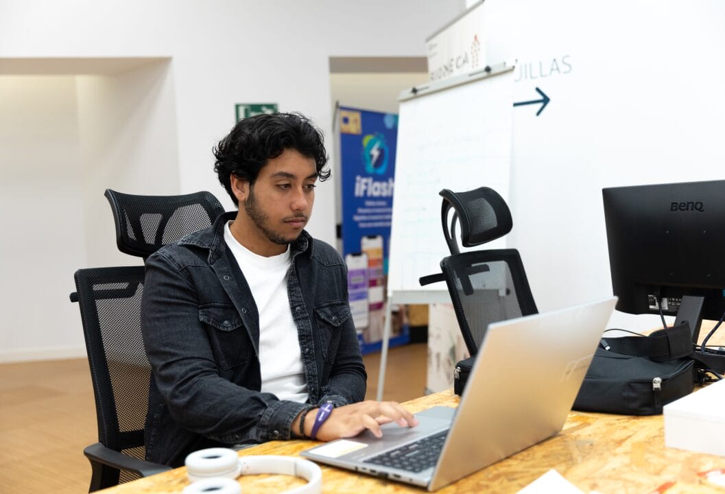 Plano medio de un emprendedor de El ángulo sentado utilizando su ordenador portátil, haciendo uso del prompt engineering en herramienta de IA.