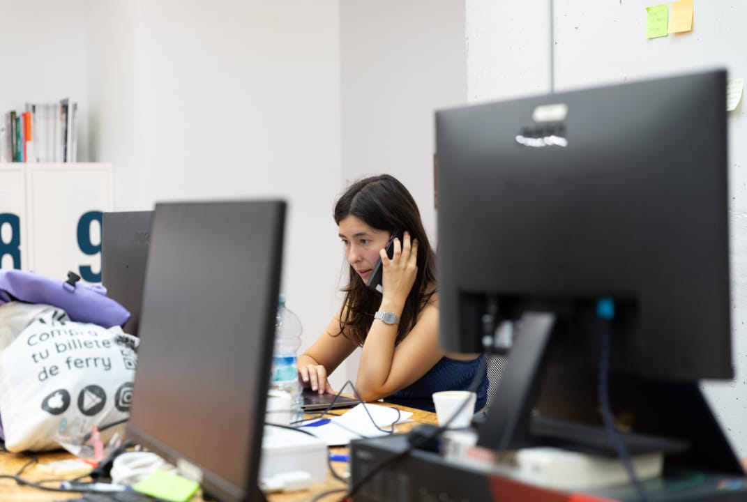 Emprendedora de Ceuta Open Future sentada habla por teléfono y trabaja en su ordenador.